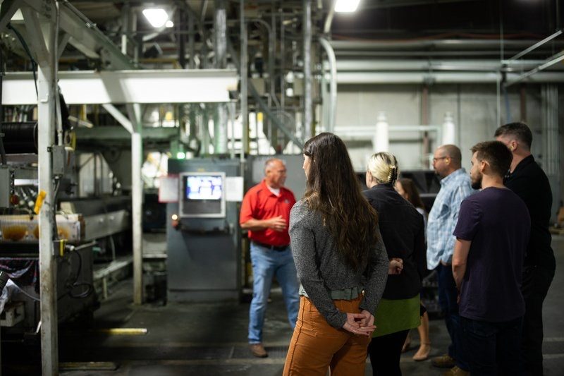 Group standing among machinery on a factory floor while a guide in red speaks