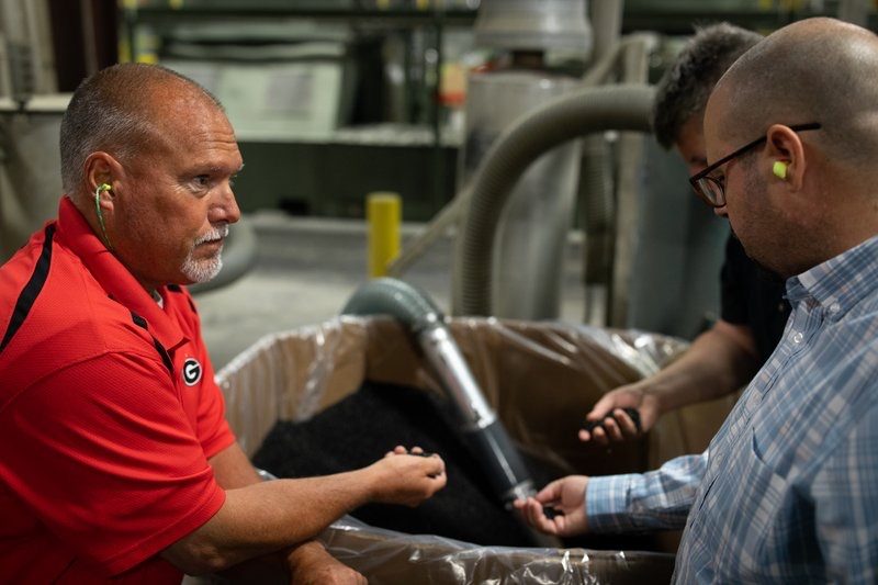 Client in a red shirt explaining a machine to two team members