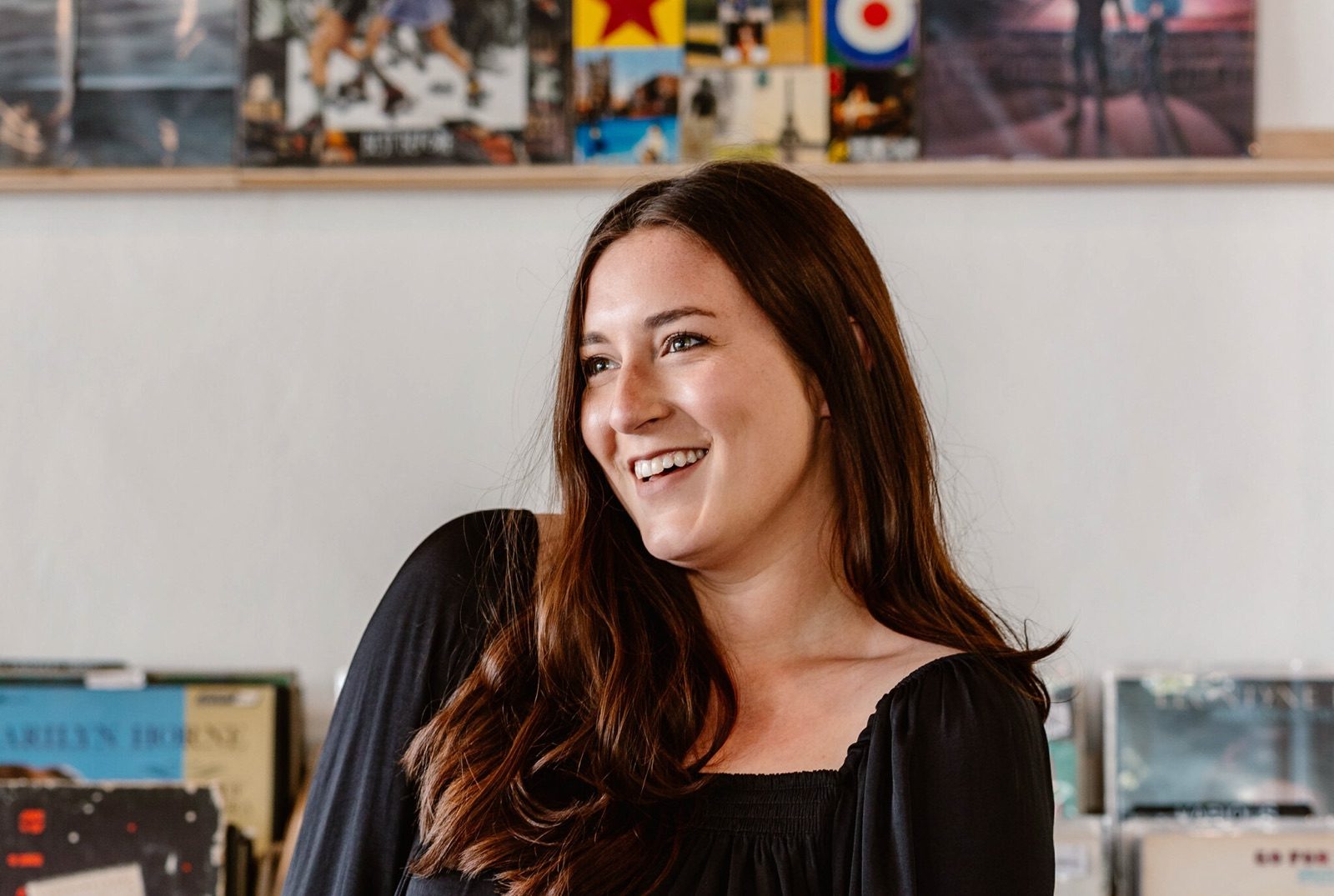 Kelli Woodell in a black top smiling in front of a wall of art prints