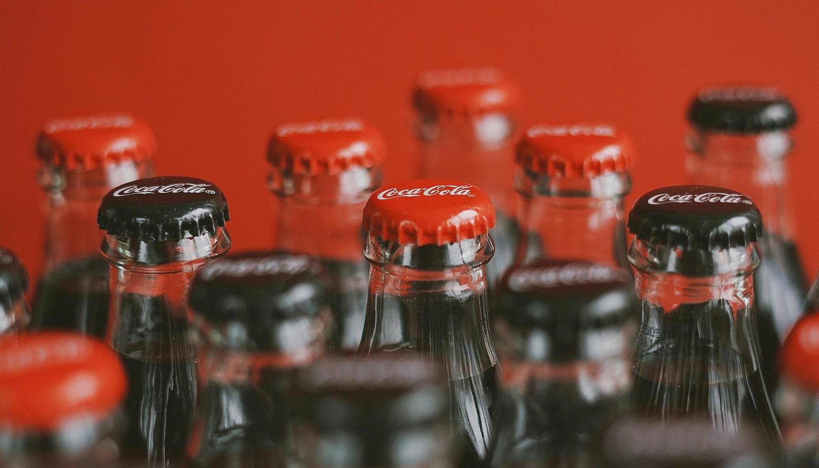 Rows of Coca-Cola bottle caps in close-up against a red background