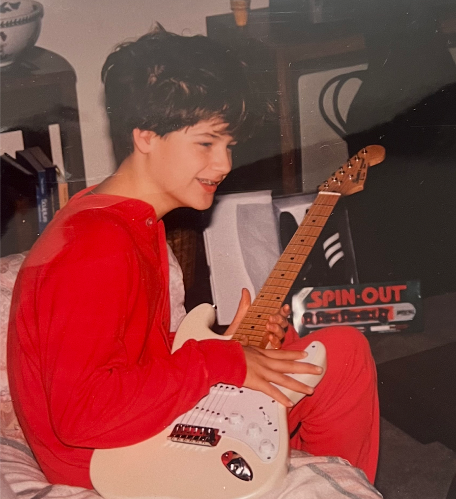 A boy in red pyjamas holding a new white electric guitar