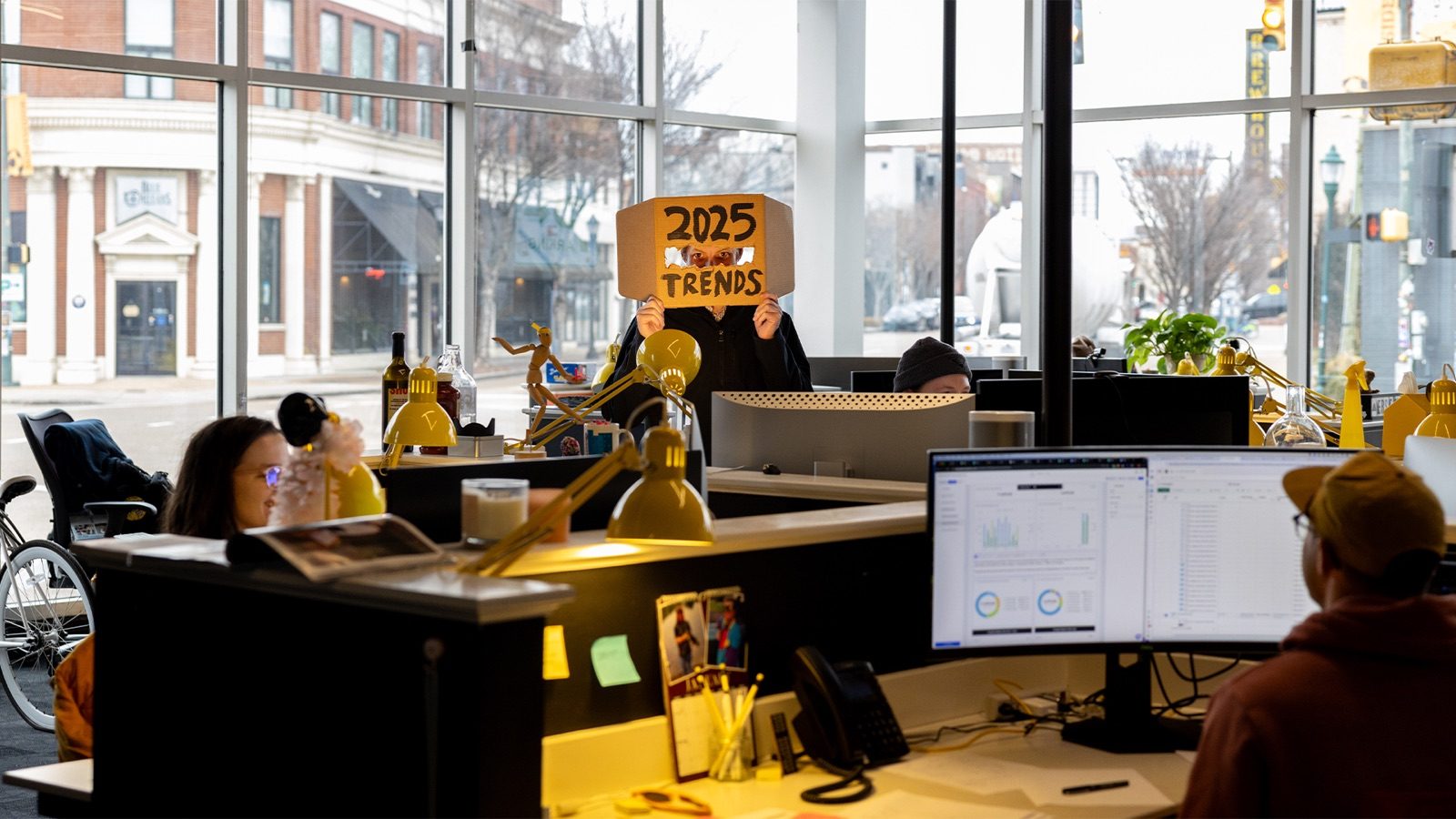 A team member holding up a hand-lettered '2025 Trends' sign in the agency's front office