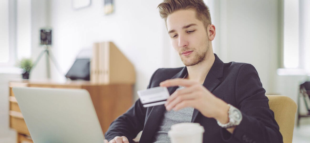 Young man at a laptop holding a credit card