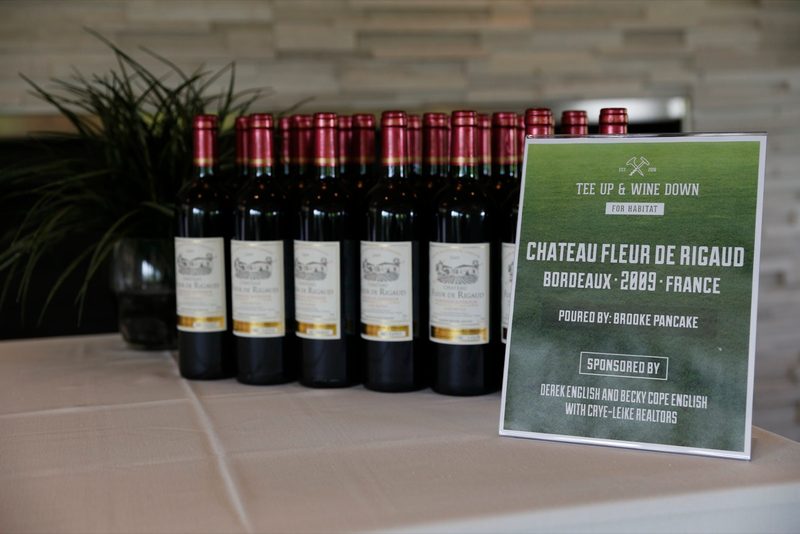 Bottles of Chateau Fleur de Rigaud Bordeaux beside a Tee Up & Wine Down sponsor sign