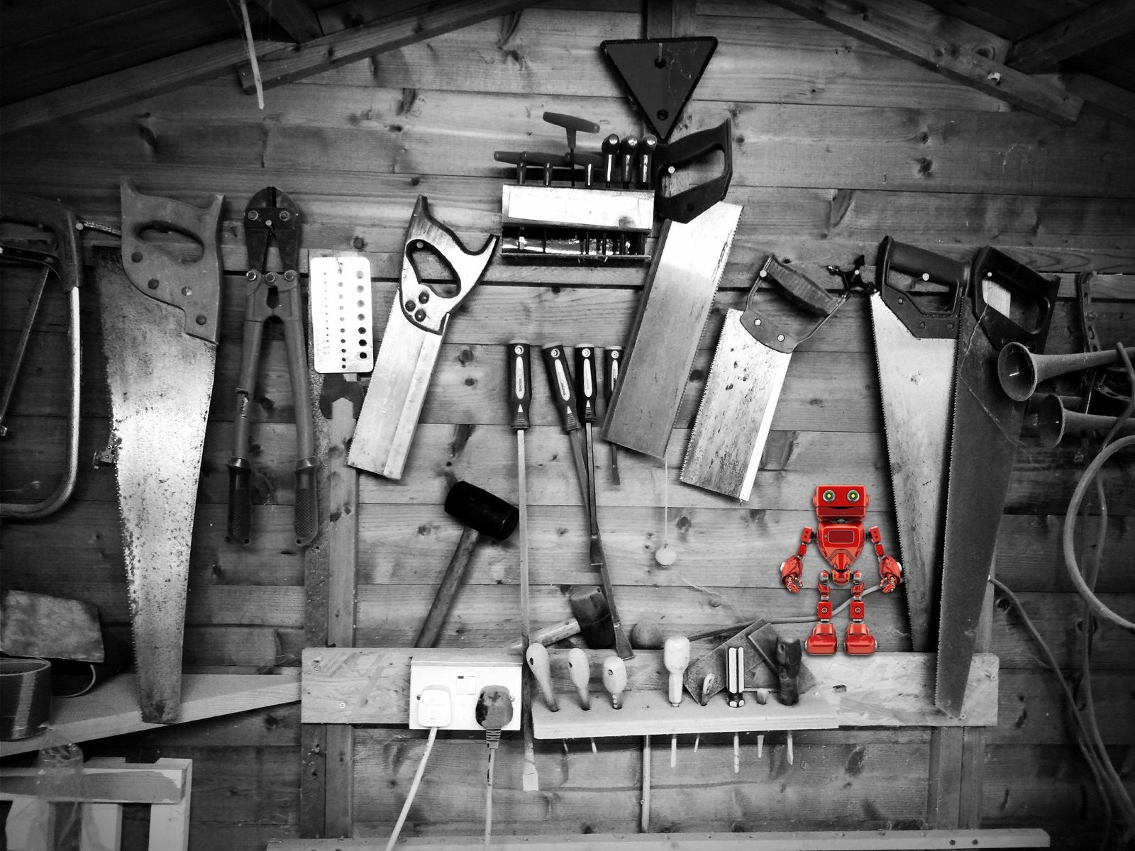 A black and white workshop wall of hand tools with a single red toy robot standing out in colour
