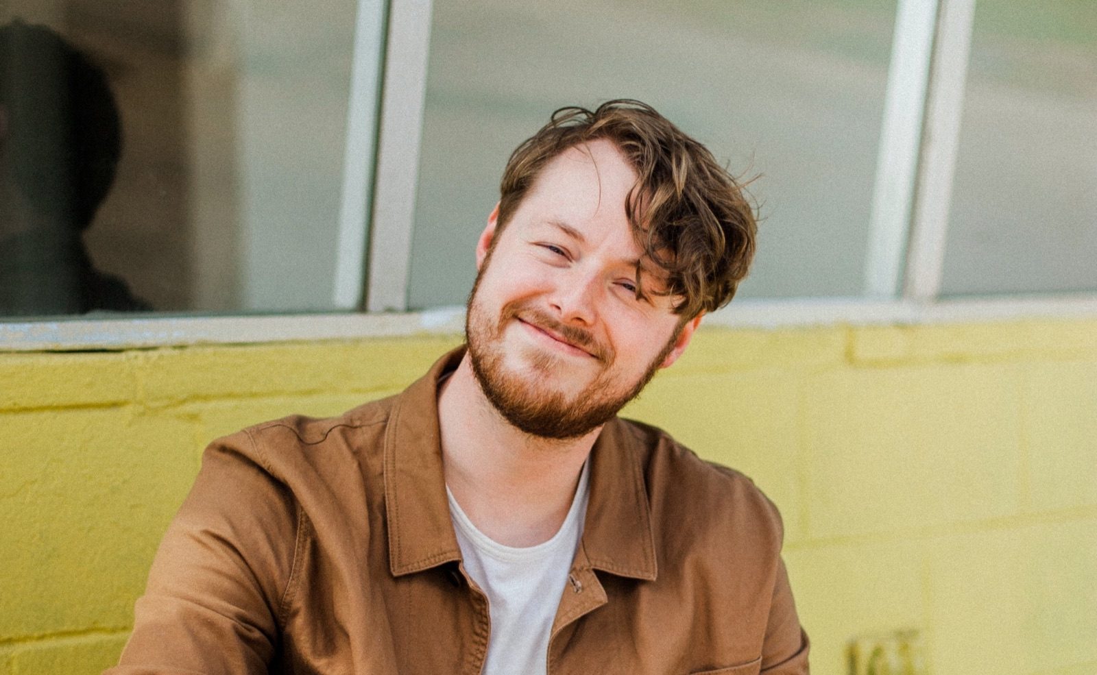 Daniel Jackson smiling in a brown jacket against a yellow wall
