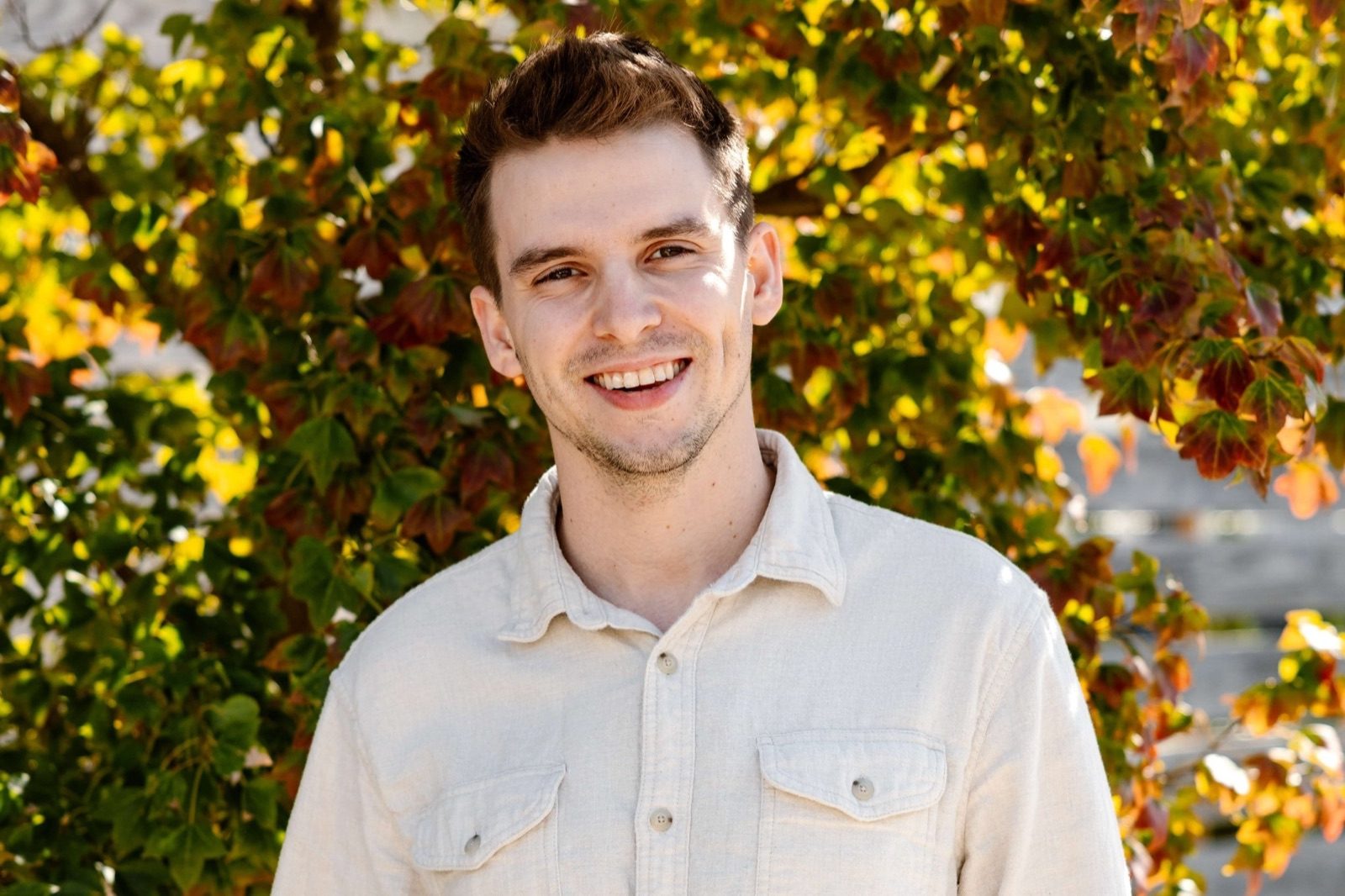 Shawn Tarr in a cream shirt smiling in front of autumn foliage