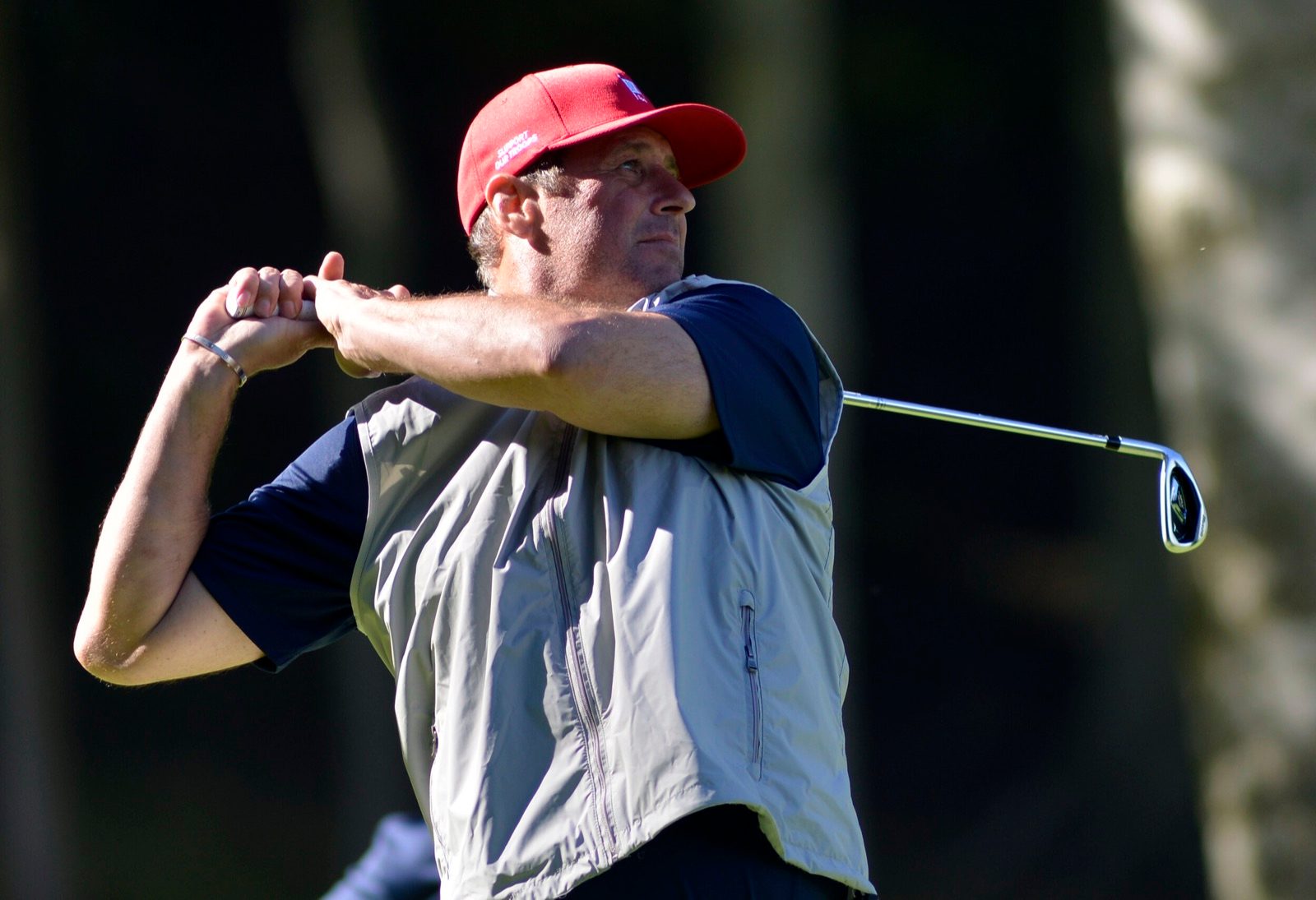 Golfer in a red cap following through on a swing