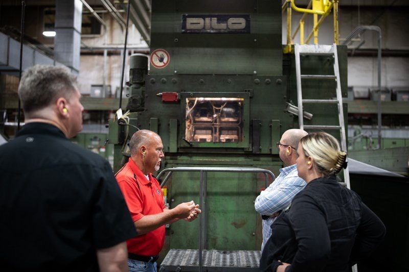 Team members listening to a client in a red shirt beside a large industrial machine