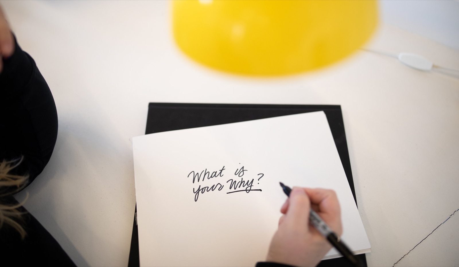 Hand writing What is your Why on a notepad under a yellow lamp