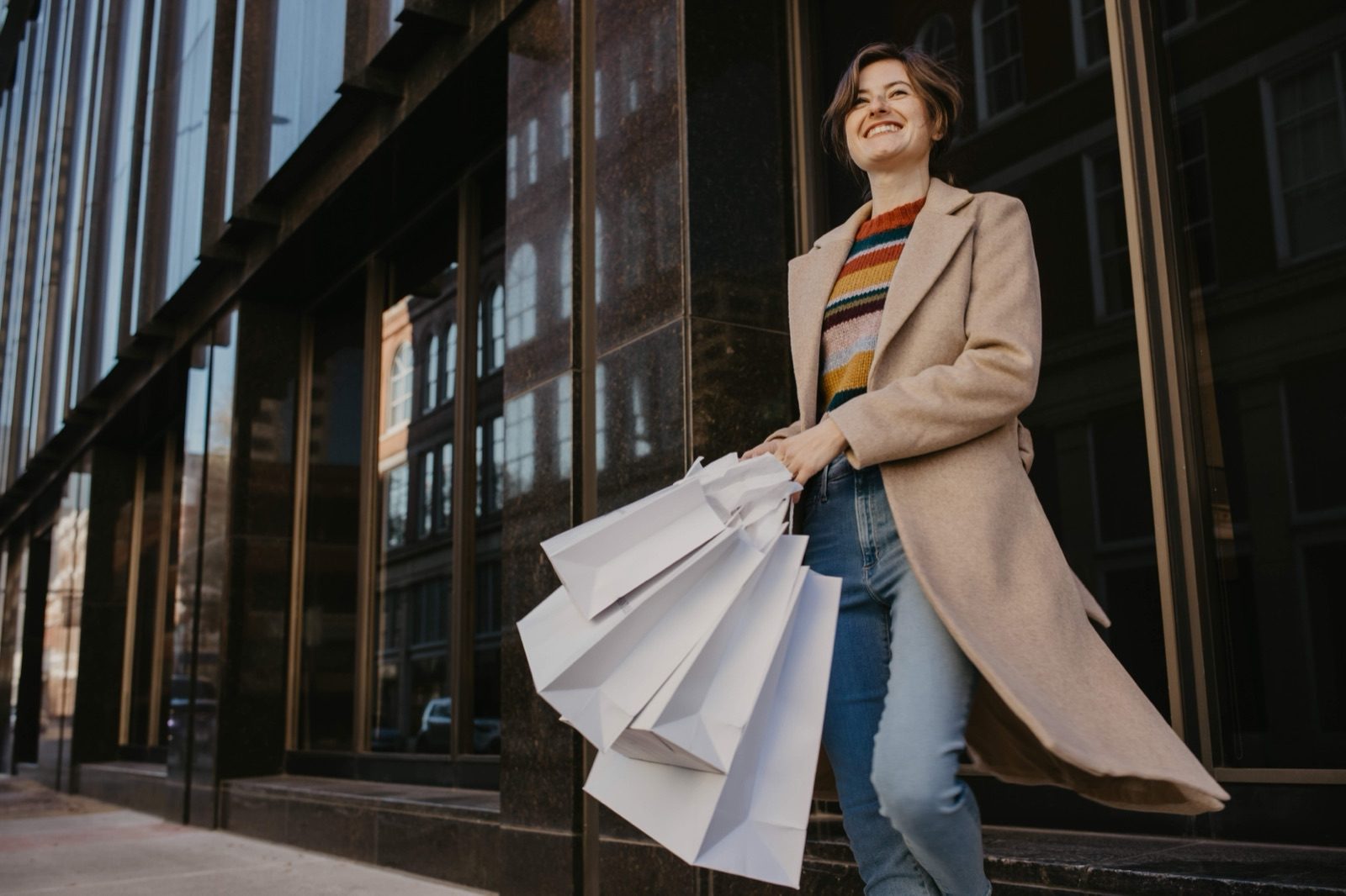 A woman with shopping bags walking past a dark glass storefront