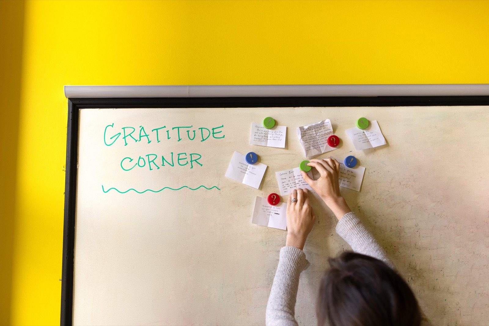 Person pinning notes to a whiteboard labeled Gratitude Corner