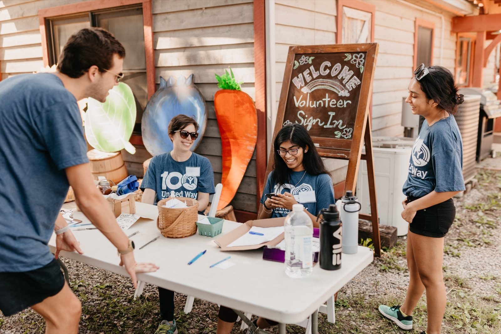 Volunteers signing in at a folding table beside a chalkboard reading 'Welcome volunteers'
