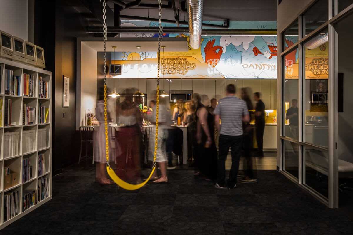 Guests mingling in the Maycreate office with a yellow swing in the foreground