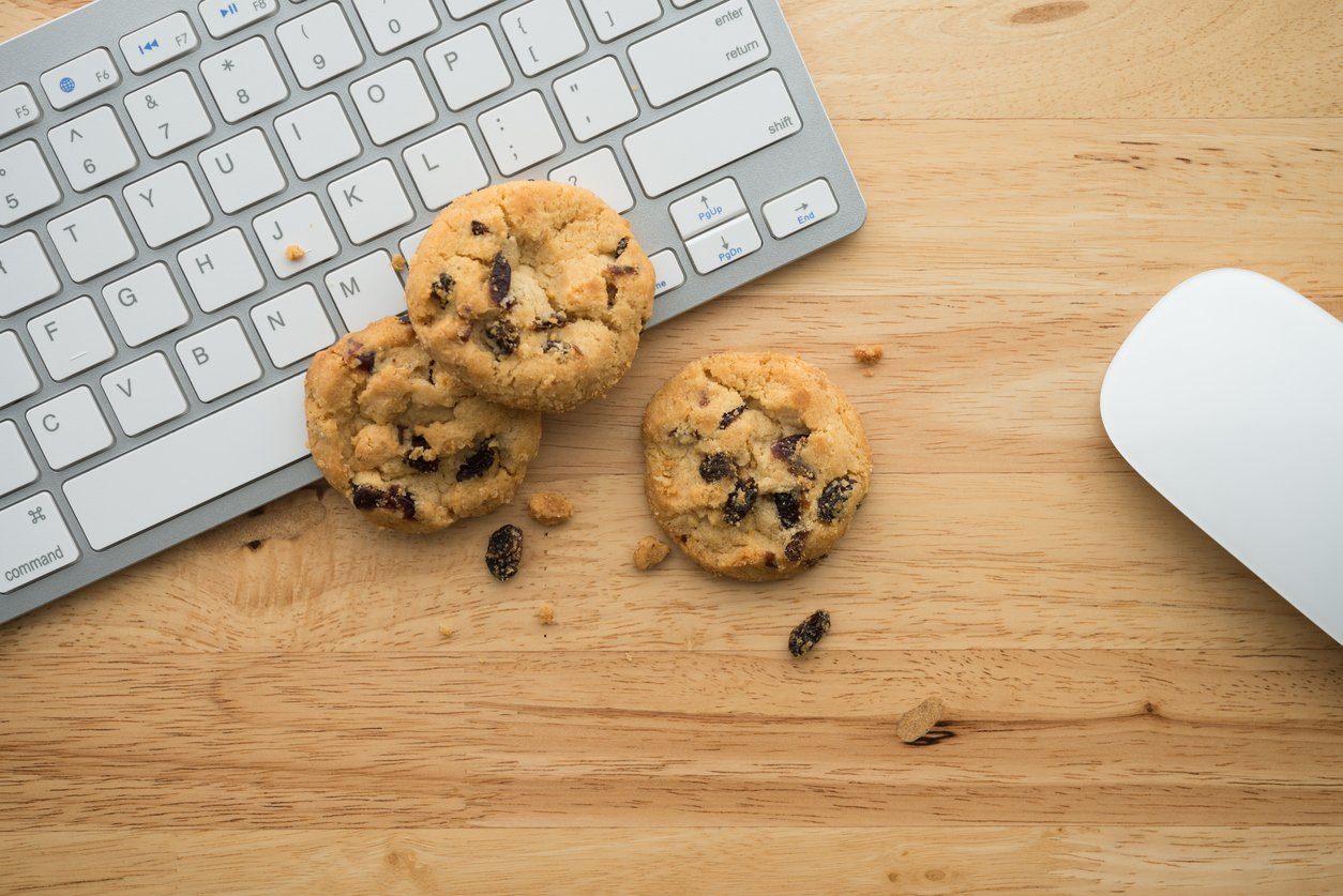 Chocolate chip cookies beside a keyboard and mouse on a wooden desk