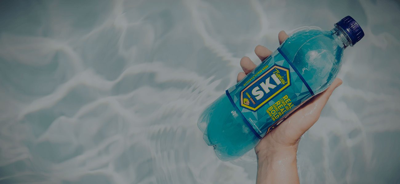 Hand holding a blue SKI soda bottle above rippling water