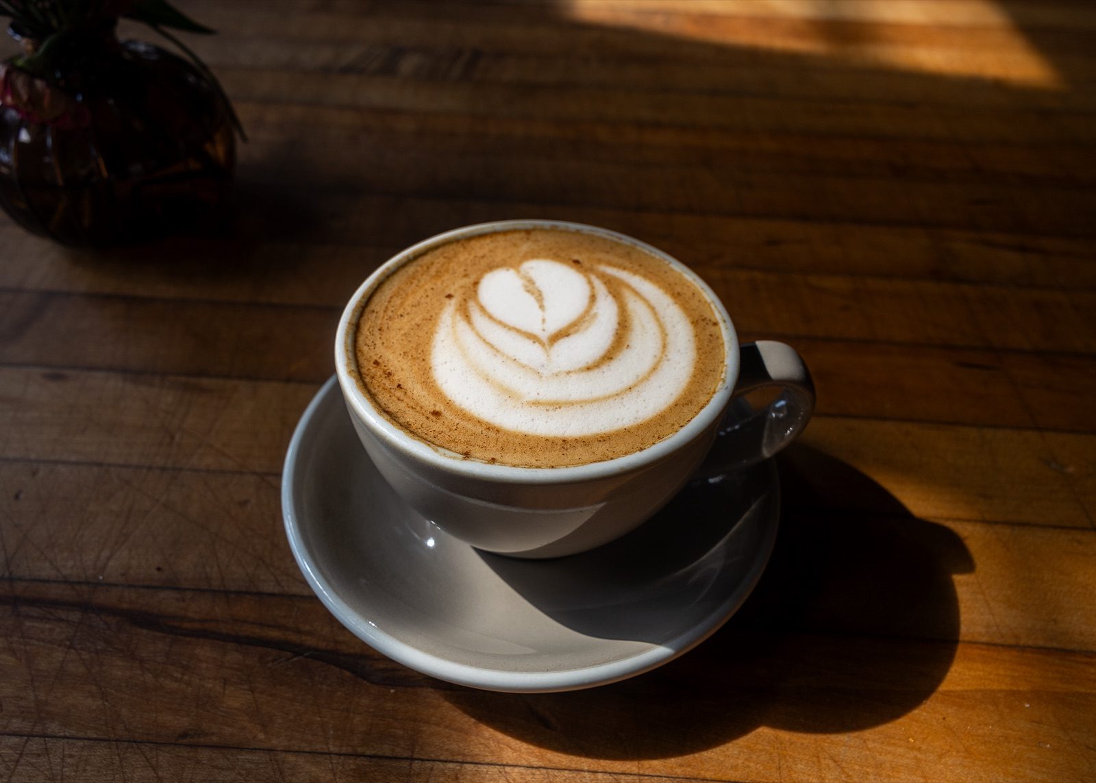 A latte with layered rosette art in a white cup on a wooden table
