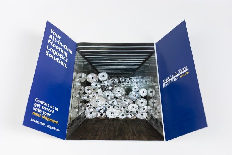 Blue trifold mailer for XGS opening to reveal a trailer full of flooring rolls
