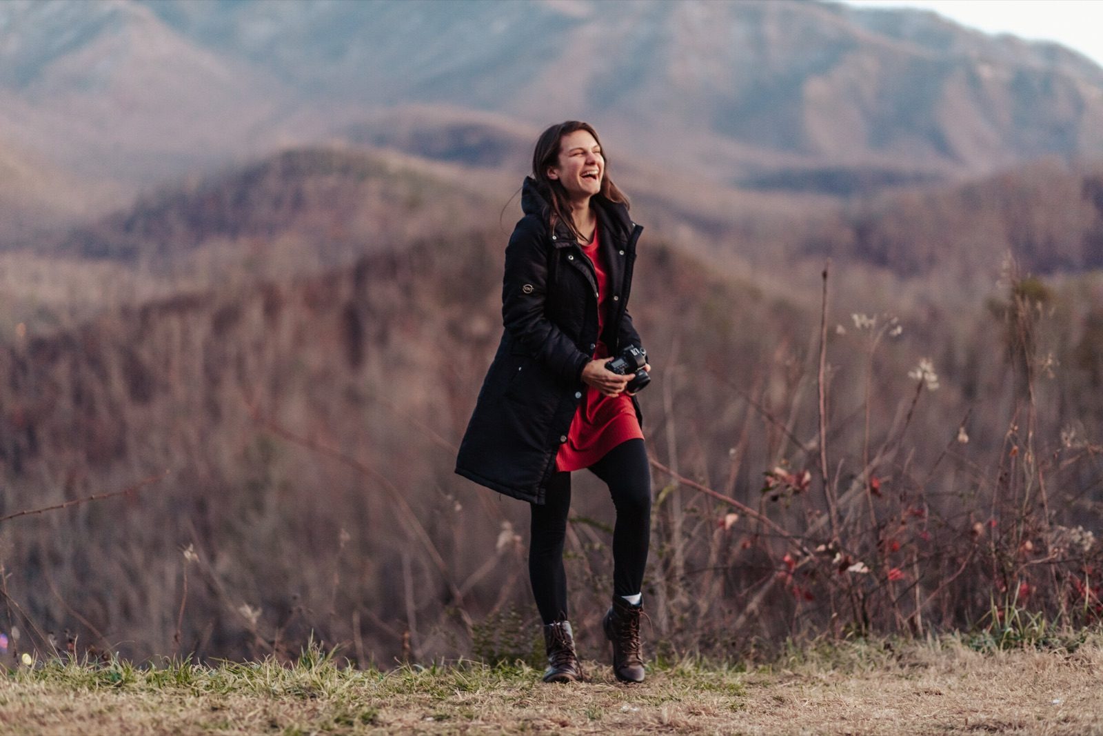 Sarah Swainson in a black coat holding a camera at a mountain overlook