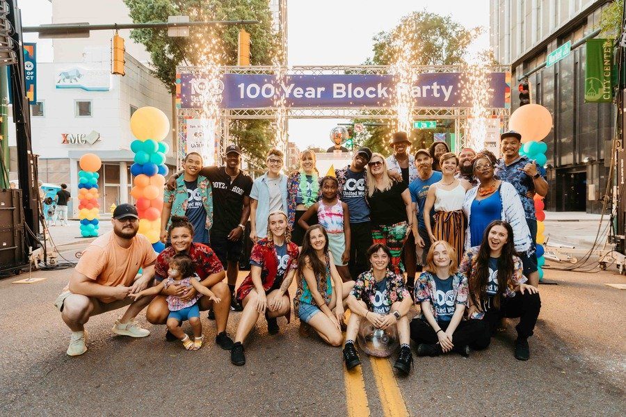 A group photograph of volunteers under the 100 Year Block Party arch