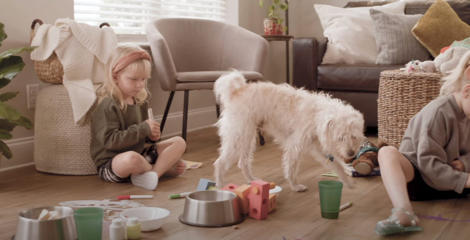 Two children playing on a living room floor with a shaggy white dog