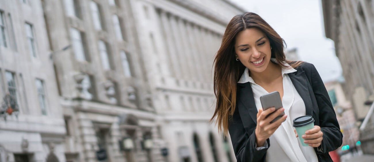 Woman in a blazer smiling at her phone on a city street