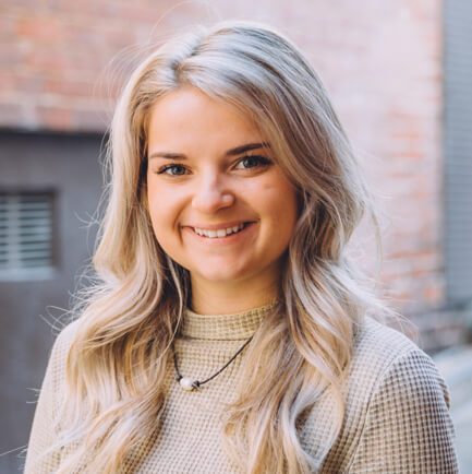 Blonde woman in a cream sweater smiling on a city sidewalk