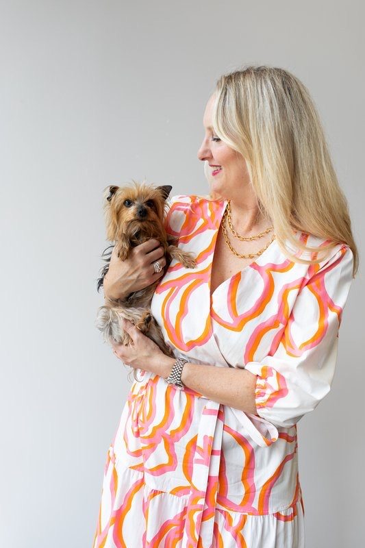 Woman in an orange and pink dress holding a small Yorkshire terrier