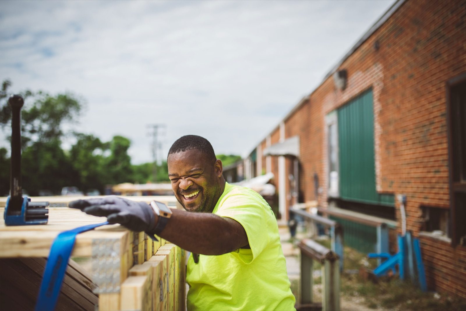 A worker in a high-visibility shirt smiling while assembling a timber frame outdoors