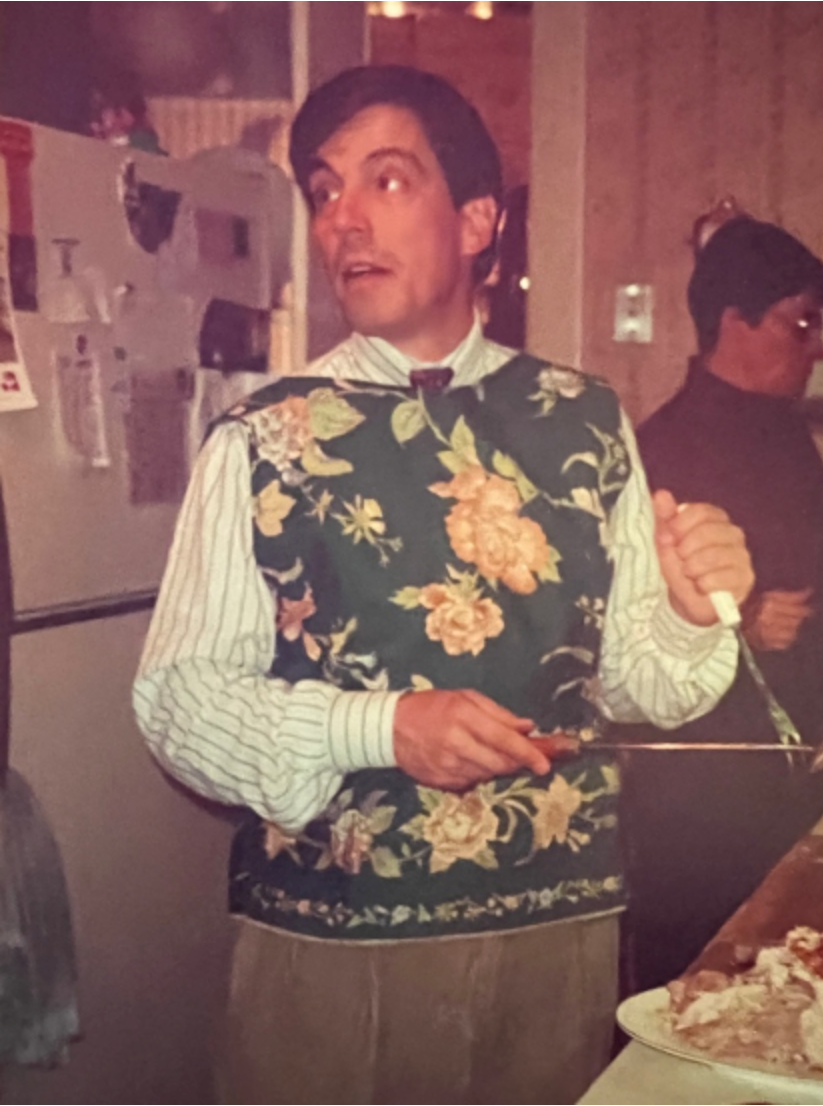 A man in a floral sweater vest carving at a holiday table