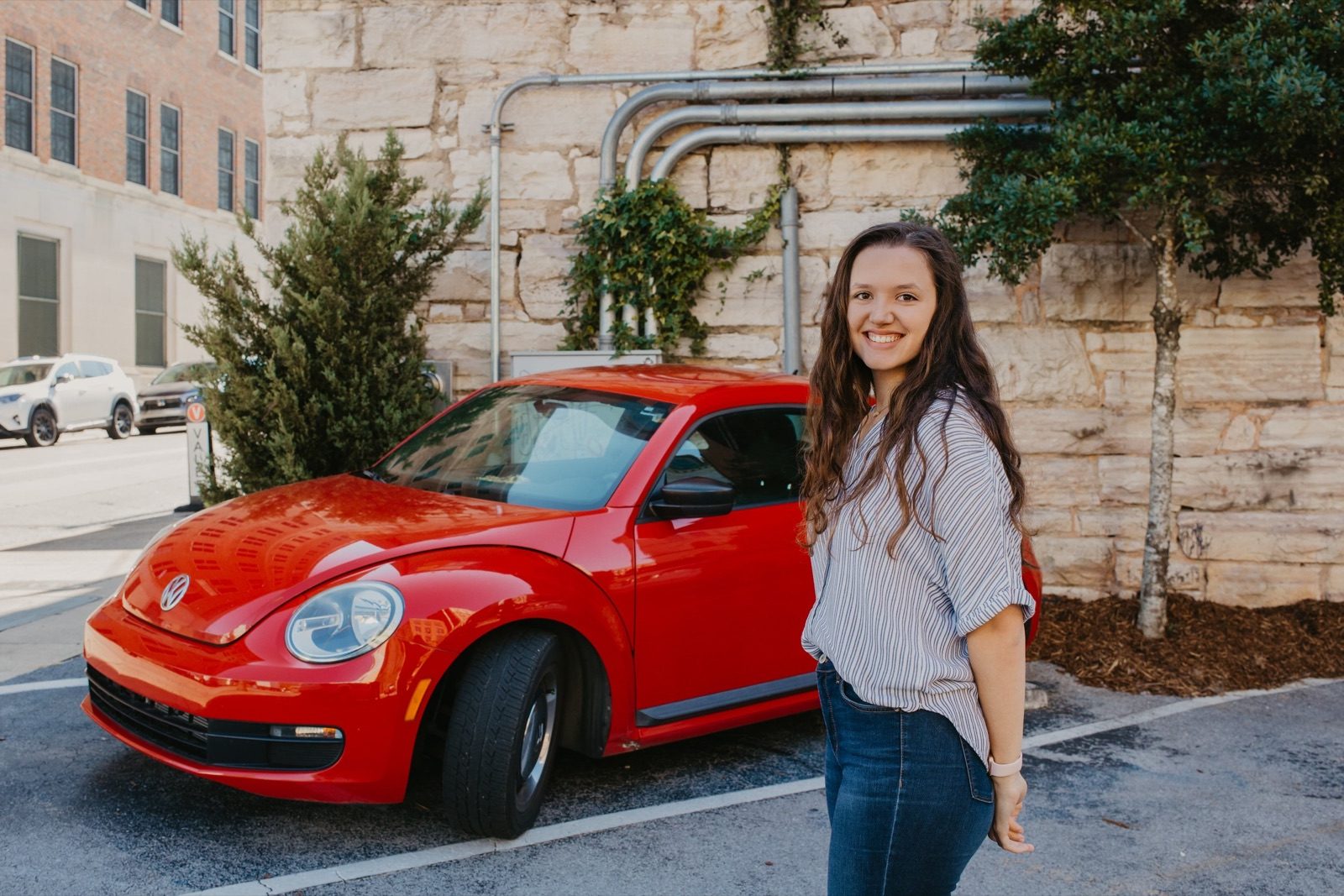 Amelia standing beside a red Volkswagen Beetle in a downtown parking lot