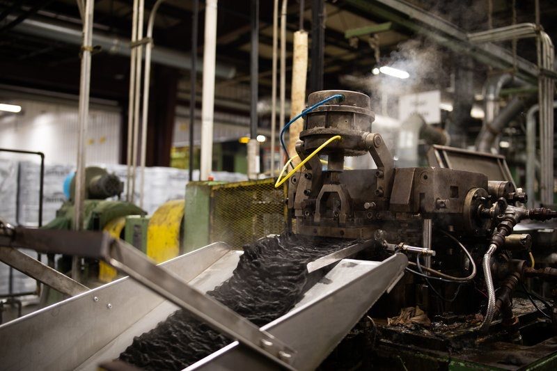 Steam rising from a machine as black fiber feeds along a conveyor