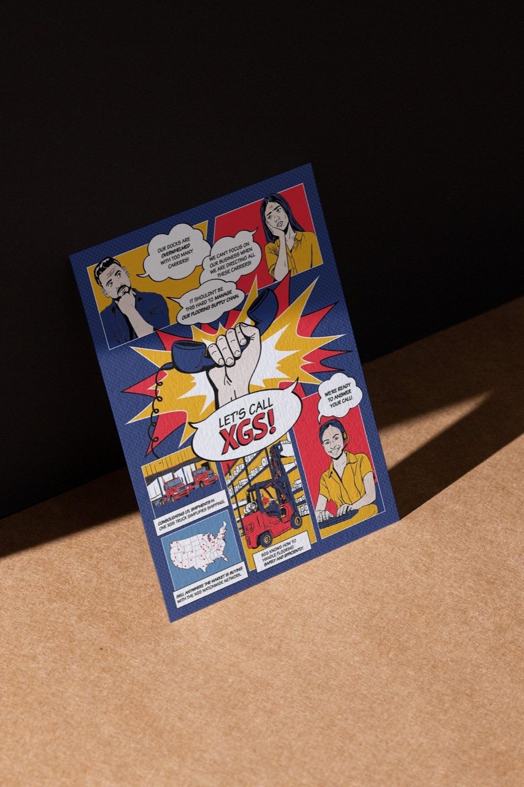 A folded XGS comic-book handout standing on a tan surface