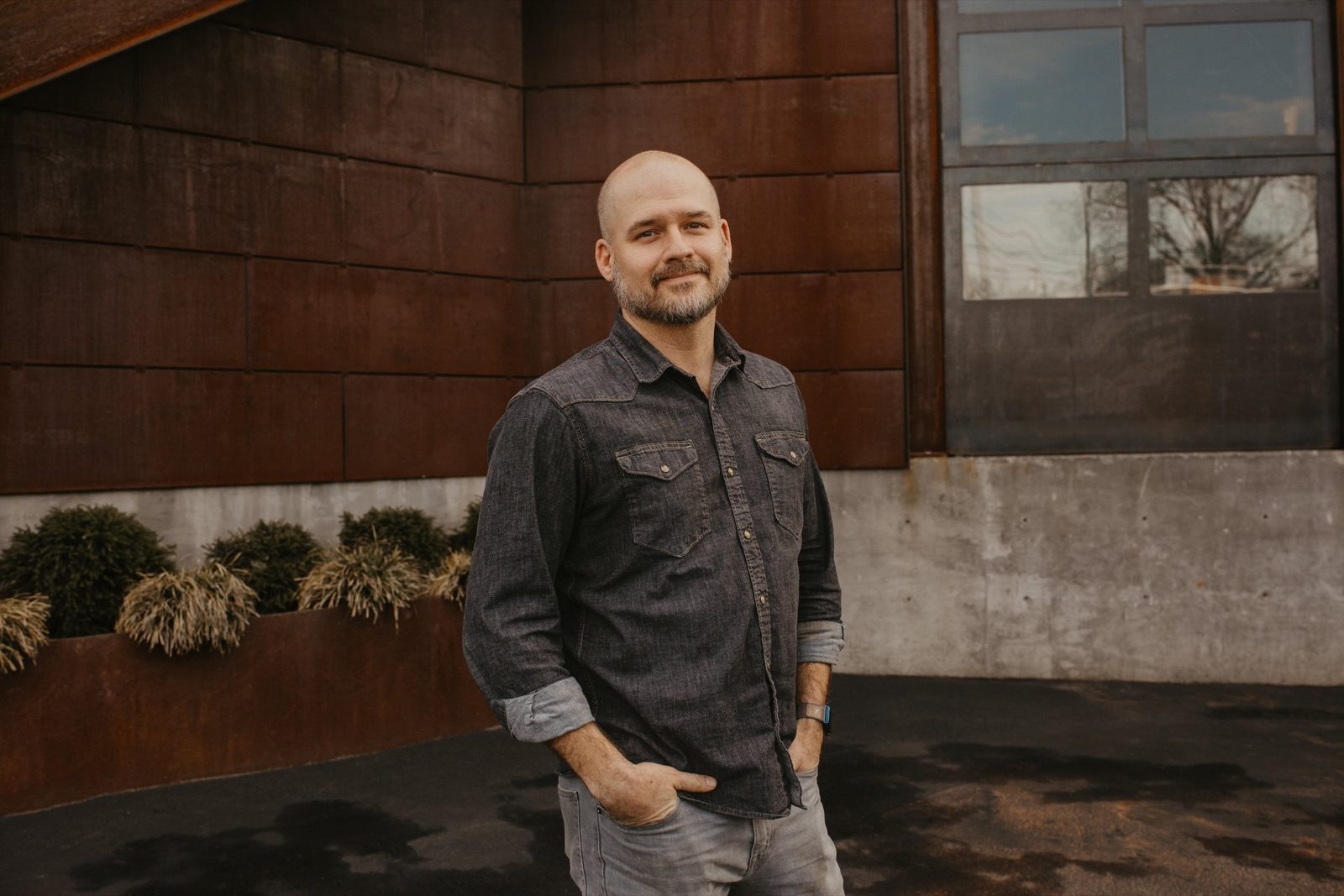 Aaron Petticord in a dark denim shirt outside a brick and glass building