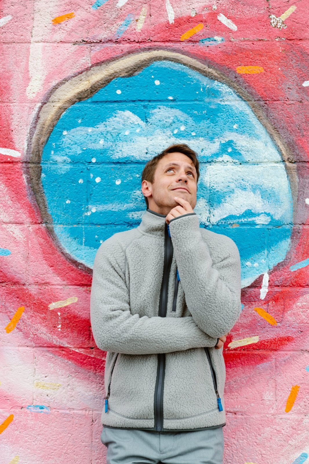 Andrew Woods in a gray hoodie posing thoughtfully in front of a colorful mural