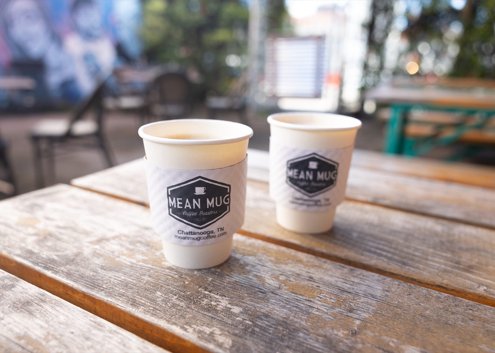 Two Mean Mug paper coffee cups on a weathered picnic table