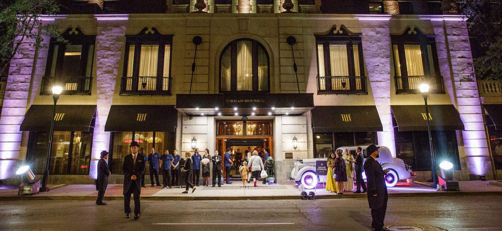 Read House hotel facade lit purple at night with guests and vintage cars out front