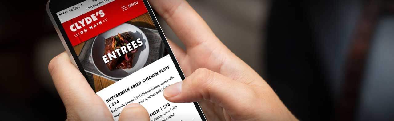 Hand holding a phone showing the Clyde's on Main entrees menu