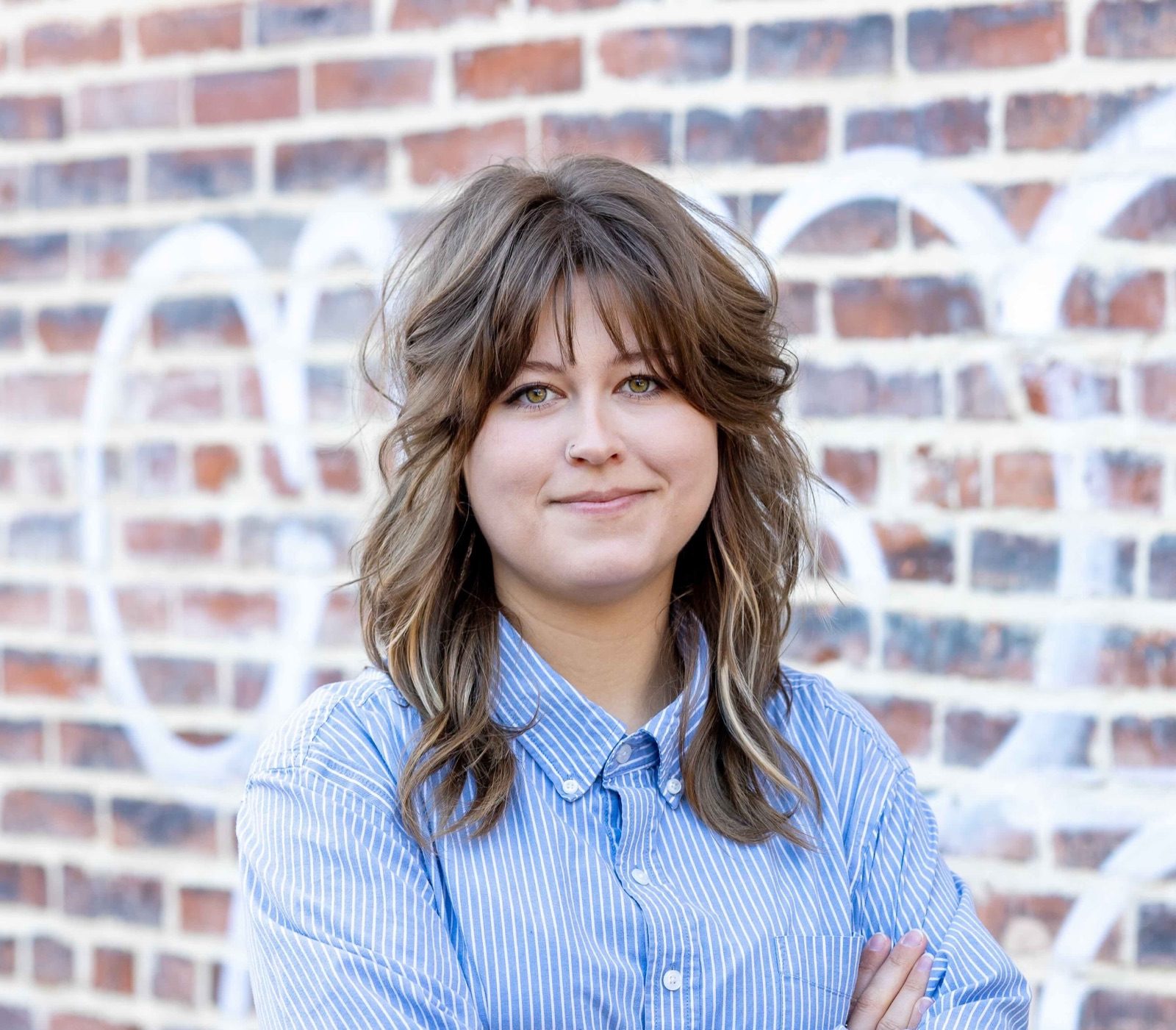 Lizzy Bigelow standing with her arms folded in front of a brick wall painted with white script