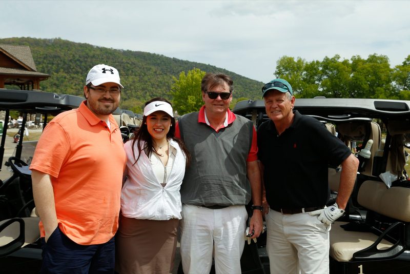 Four golfers posing in front of golf carts