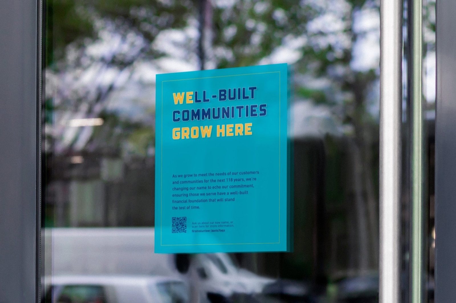 Teal poster in a bank window reading Well-Built Communities Grow Here