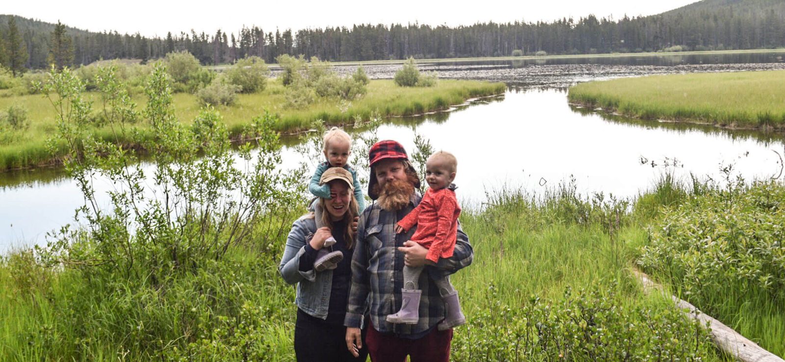 Alex DeHart and family standing beside a marsh with pines behind