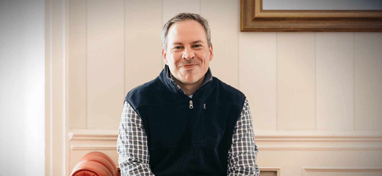 Brian Murphy in a fleece vest smiling in a wood-paneled room