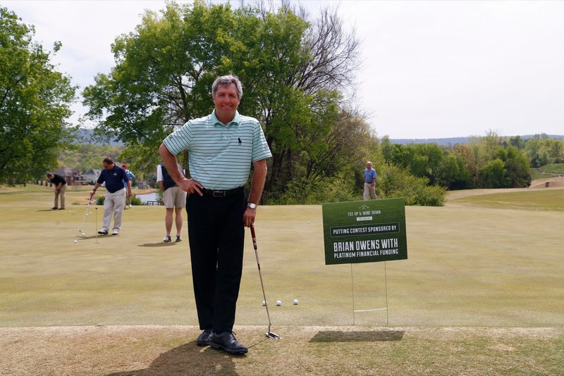 Golfer posing beside a sponsor sign on the course