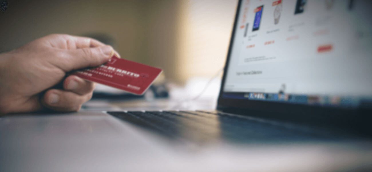 Hand holding a red credit card at a laptop showing an online store