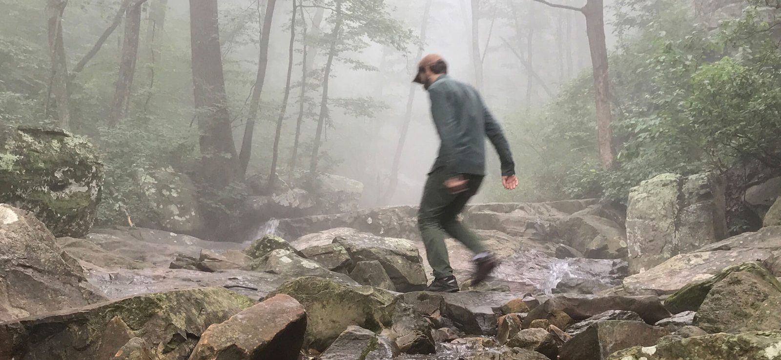 Adam Ewing hiking across mossy boulders in a foggy forest