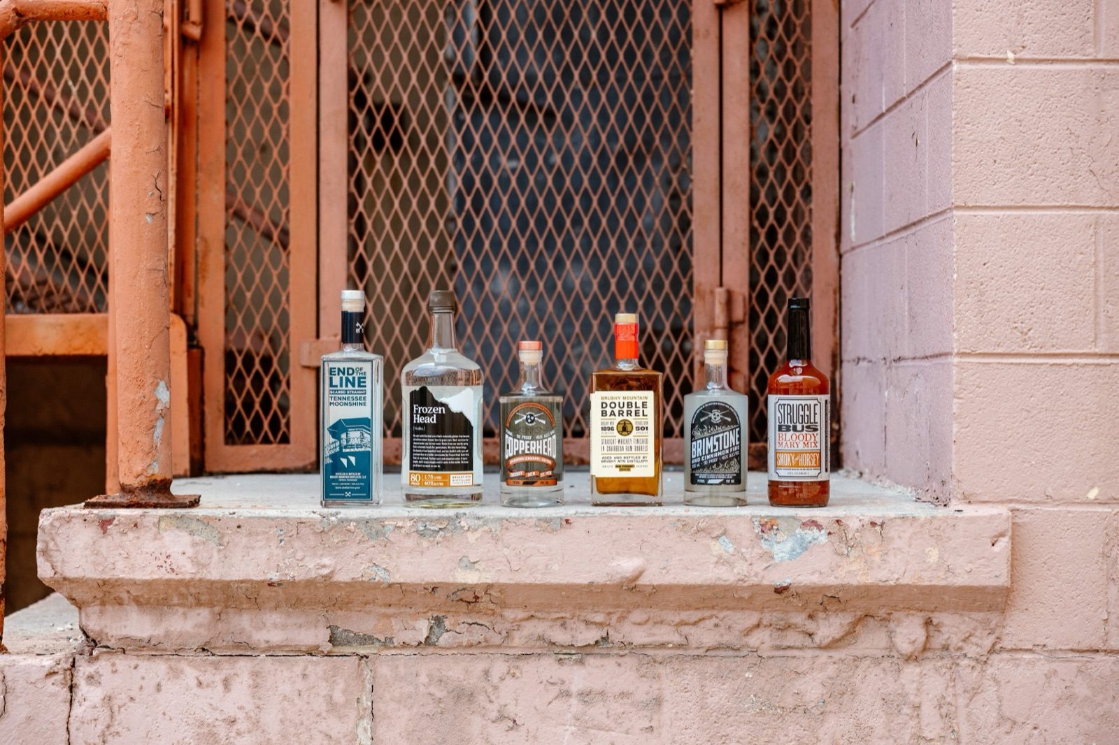 Six spirits bottles with different label designs lined up on a weathered concrete ledge
