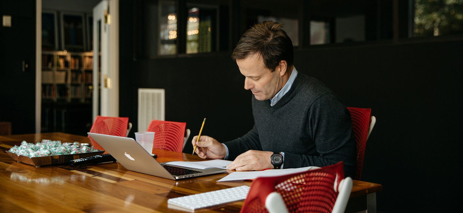 John Wagoner working at a laptop in a conference room with red chairs