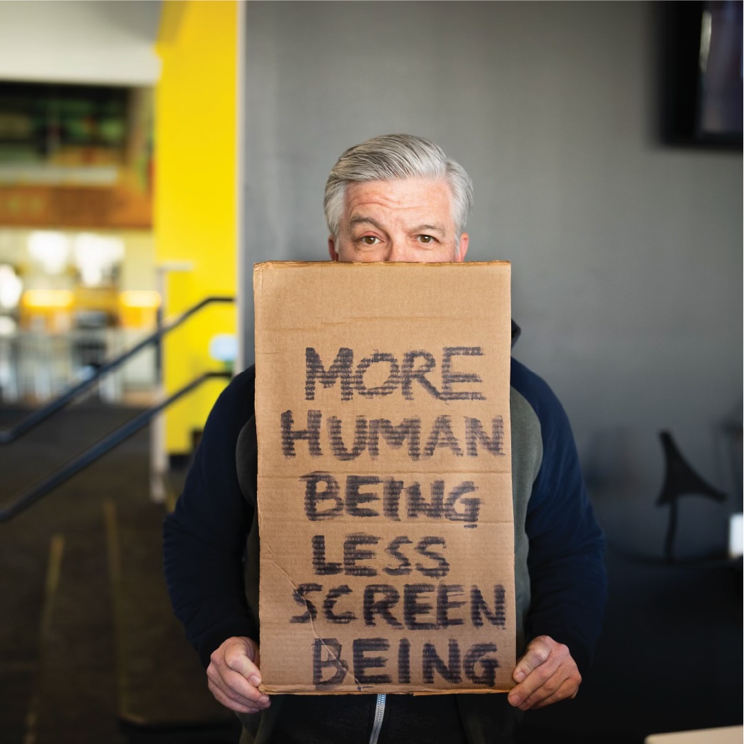 Brian holding a sign reading More Human Being, Less Screen Being